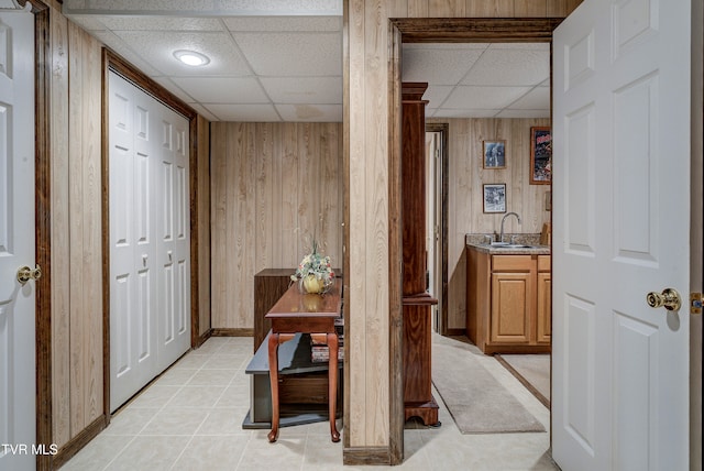 hall featuring a paneled ceiling, wooden walls, and sink