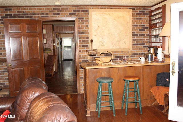 kitchen featuring dark hardwood / wood-style flooring, kitchen peninsula, a breakfast bar, and brick wall