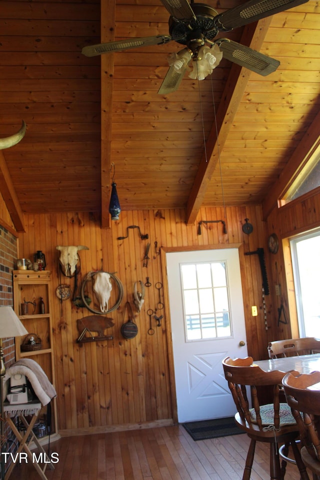 dining room with hardwood / wood-style flooring, wooden walls, and vaulted ceiling with beams