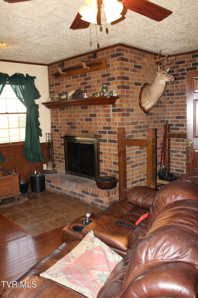 living room with a brick fireplace, hardwood / wood-style flooring, ceiling fan, and a textured ceiling