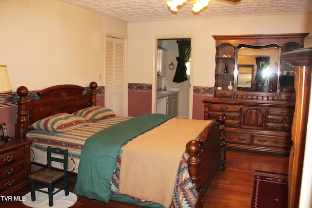 bedroom with ensuite bath, dark wood-type flooring, a textured ceiling, and a closet