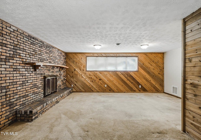 unfurnished living room with a textured ceiling, light colored carpet, a brick fireplace, and wood walls