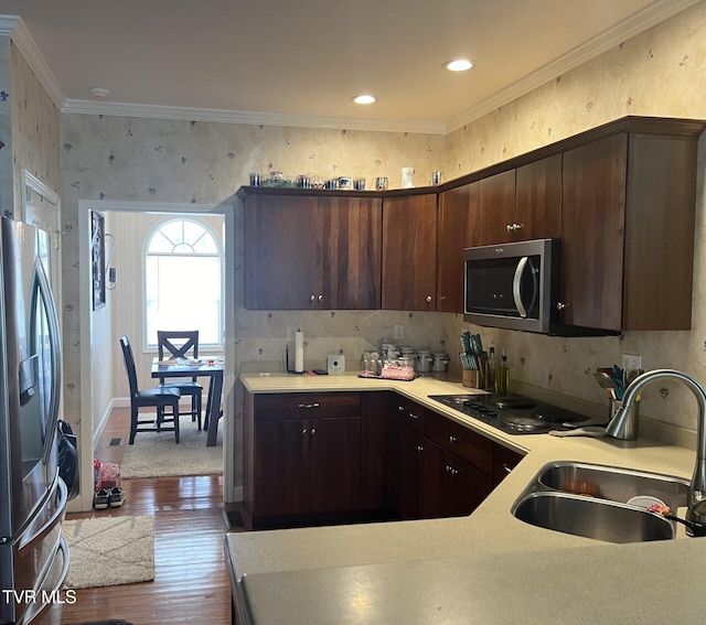 kitchen with sink, appliances with stainless steel finishes, hardwood / wood-style floors, dark brown cabinets, and crown molding