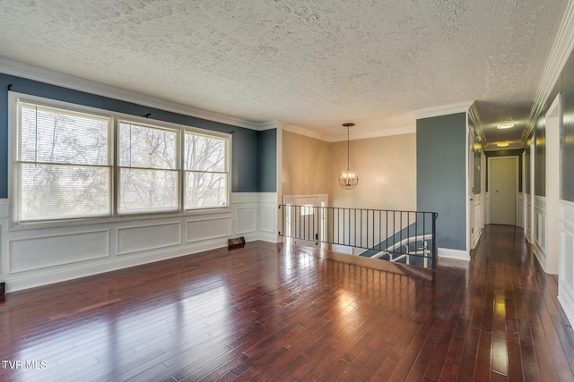 spare room with a textured ceiling, dark hardwood / wood-style floors, crown molding, and a chandelier