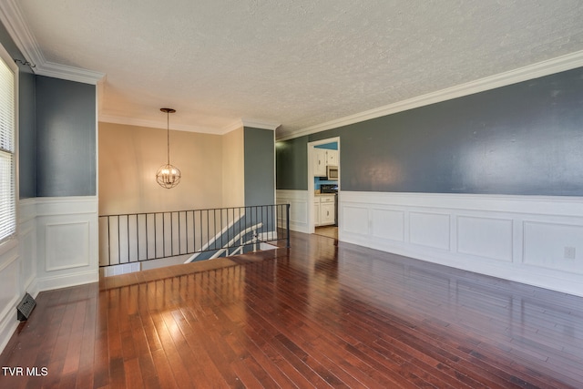 empty room featuring a textured ceiling, crown molding, dark hardwood / wood-style floors, and a notable chandelier