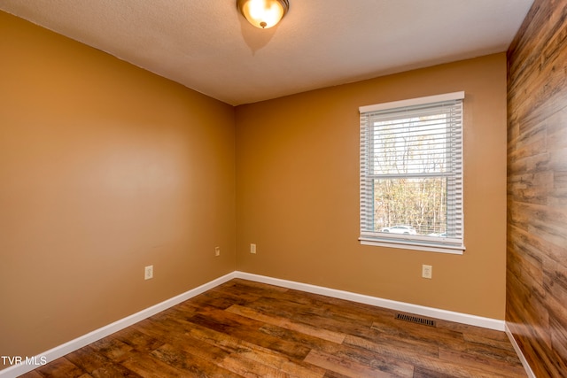 unfurnished room featuring wooden walls, a textured ceiling, and hardwood / wood-style flooring