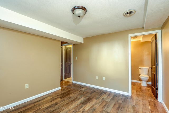 unfurnished bedroom with a textured ceiling, ensuite bath, and hardwood / wood-style flooring