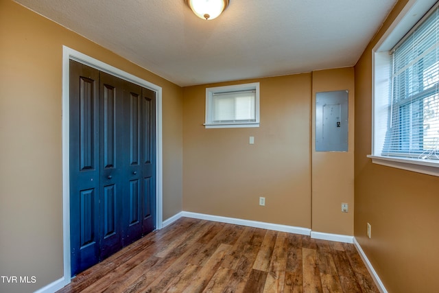 unfurnished bedroom with electric panel, hardwood / wood-style floors, a textured ceiling, and a closet