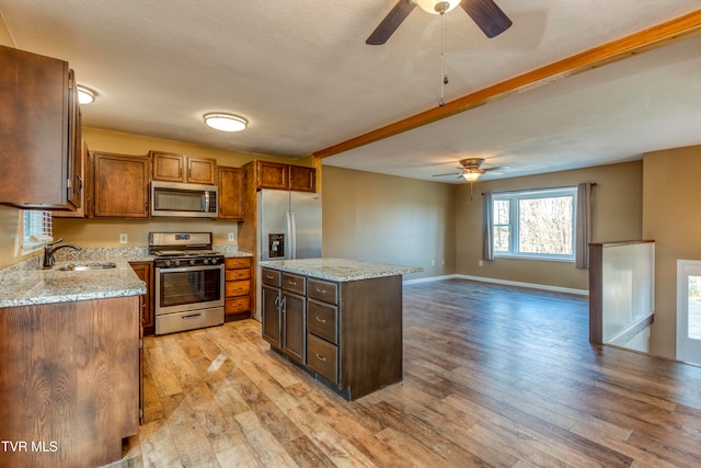 kitchen featuring stainless steel appliances, sink, ceiling fan, a center island, and light wood-type flooring