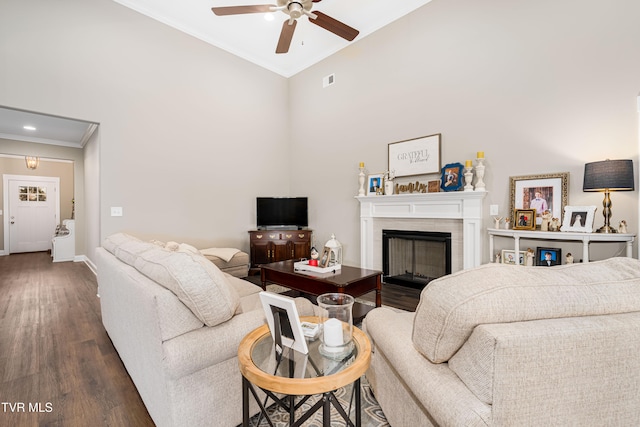 living room featuring dark wood-type flooring, a high ceiling, ceiling fan, and crown molding