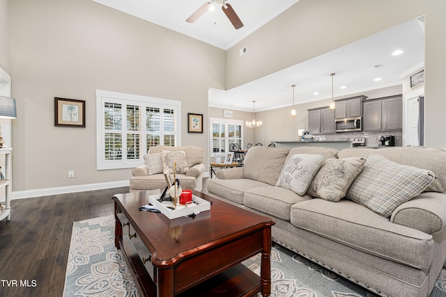 living room with dark wood-type flooring, a towering ceiling, ceiling fan with notable chandelier, and ornamental molding