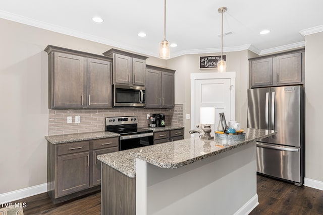 kitchen with appliances with stainless steel finishes, dark hardwood / wood-style floors, light stone countertops, hanging light fixtures, and a kitchen island with sink