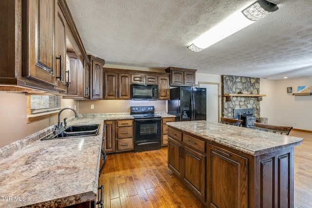 kitchen with black appliances, a textured ceiling, sink, a kitchen island, and light wood-type flooring