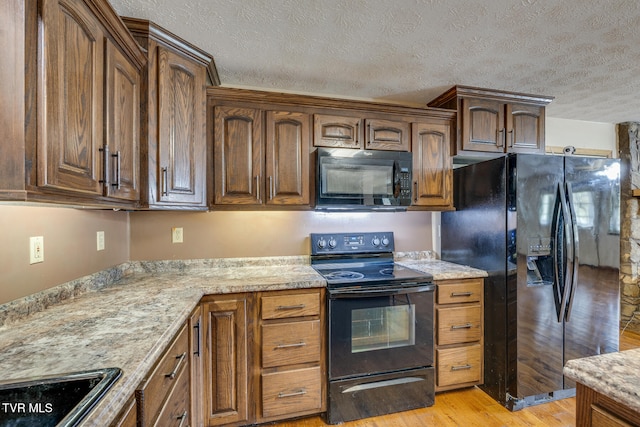 kitchen featuring black appliances, light stone countertops, a textured ceiling, and light hardwood / wood-style floors