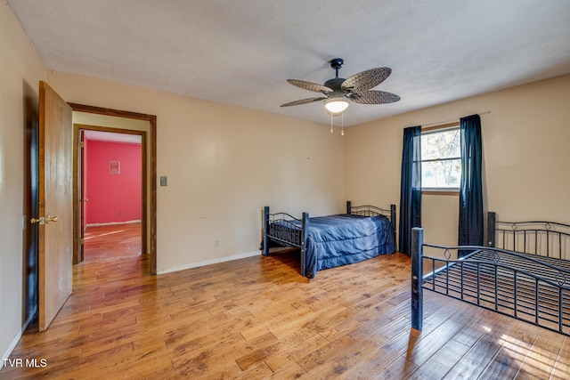 bedroom with ceiling fan, baseboards, light wood finished floors, and a textured ceiling