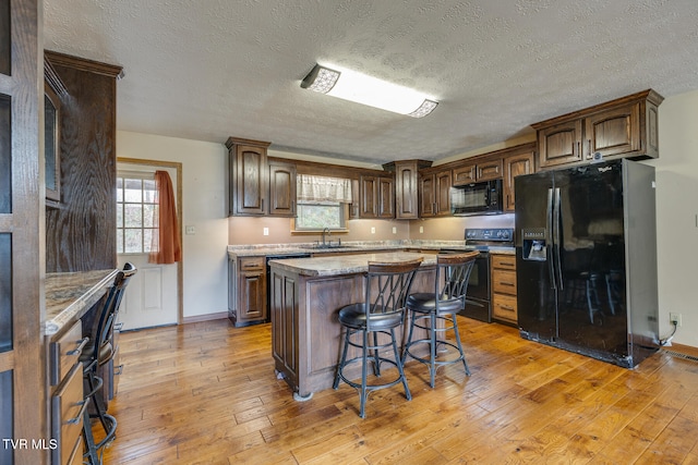 kitchen with black appliances, a breakfast bar area, a textured ceiling, a kitchen island, and light wood-type flooring