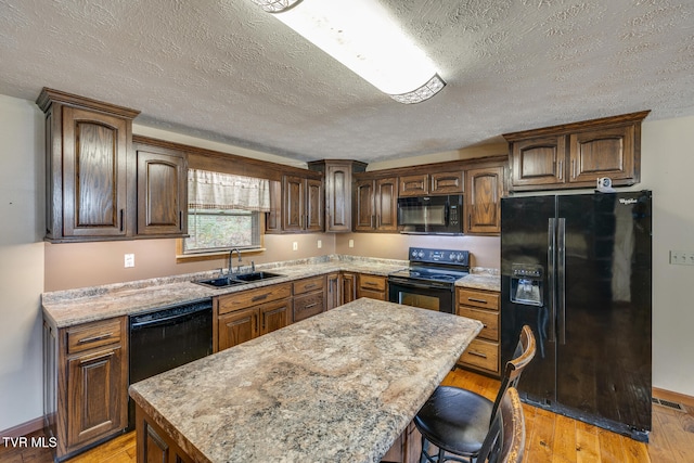 kitchen featuring a kitchen island, a breakfast bar, light wood-style flooring, black appliances, and a sink