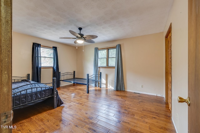 bedroom with a textured ceiling, wood-type flooring, multiple windows, and ceiling fan