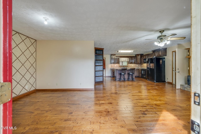 unfurnished living room featuring baseboards, a textured ceiling, light wood-type flooring, and ceiling fan