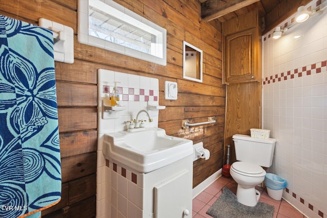 bathroom with toilet, wooden walls, tile patterned flooring, and tile walls