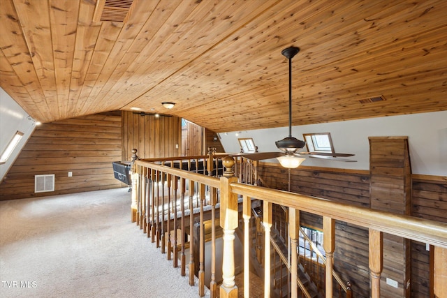 hallway featuring carpet floors, wood walls, lofted ceiling with skylight, and wooden ceiling