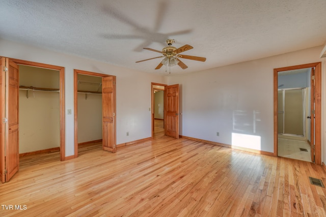 unfurnished bedroom with a textured ceiling, multiple closets, light hardwood / wood-style flooring, and ceiling fan