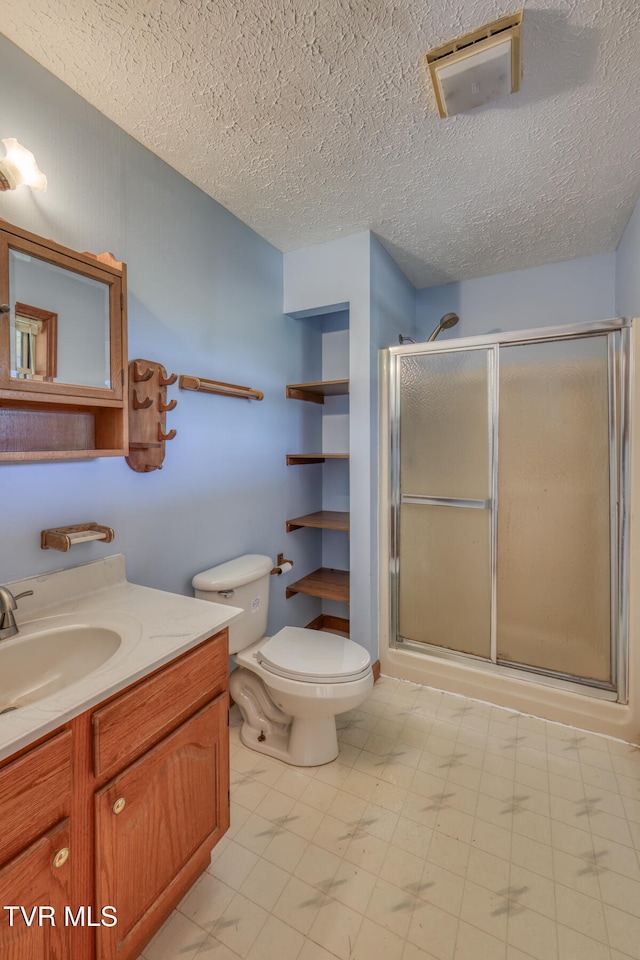 bathroom featuring vanity, a shower with door, a textured ceiling, and toilet