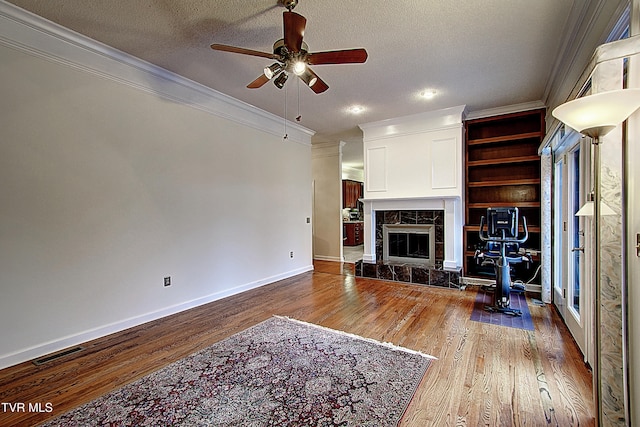 living room featuring wood-type flooring, a fireplace, a textured ceiling, and crown molding