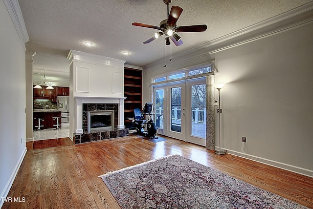 unfurnished living room with a textured ceiling, a tile fireplace, french doors, light hardwood / wood-style floors, and ceiling fan