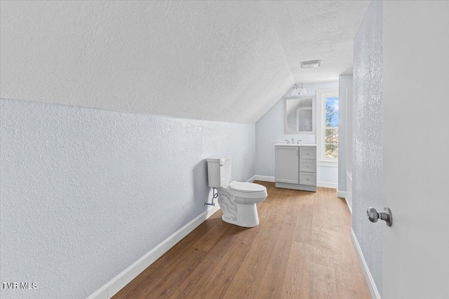 bathroom featuring vanity, a textured ceiling, vaulted ceiling, hardwood / wood-style flooring, and toilet