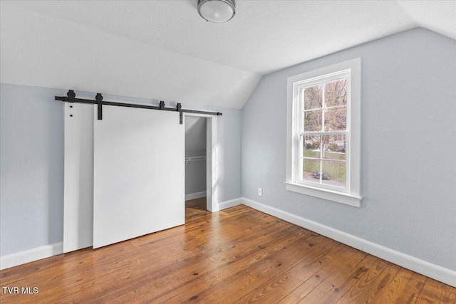 additional living space with hardwood / wood-style floors, lofted ceiling, a barn door, and a textured ceiling