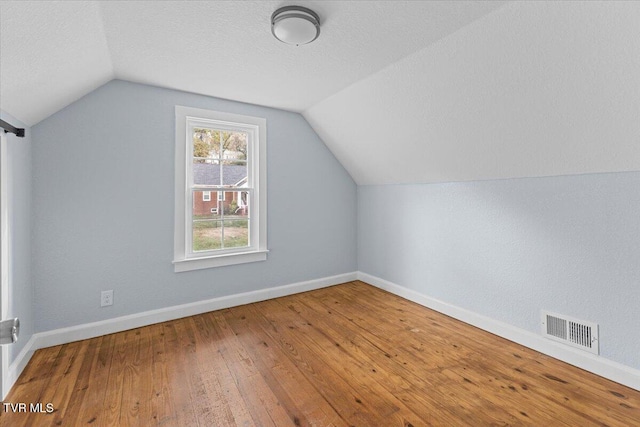 additional living space with wood-type flooring, a textured ceiling, and vaulted ceiling