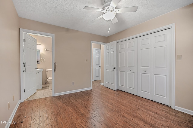 unfurnished bedroom with light wood-type flooring, ensuite bath, ceiling fan, and a closet