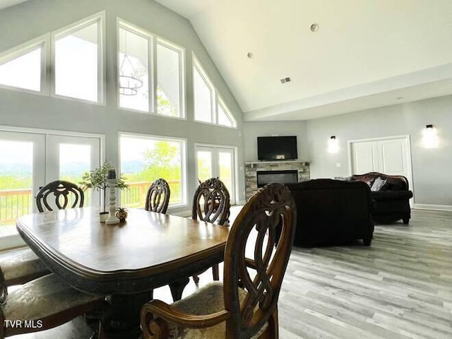 dining space with a stone fireplace, light hardwood / wood-style flooring, high vaulted ceiling, and french doors