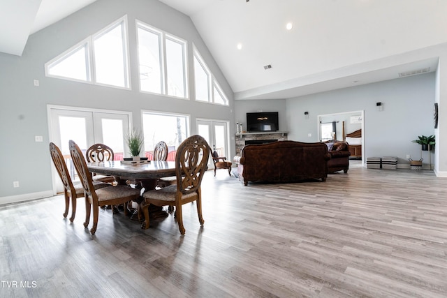 dining area featuring light hardwood / wood-style floors, a stone fireplace, high vaulted ceiling, and french doors