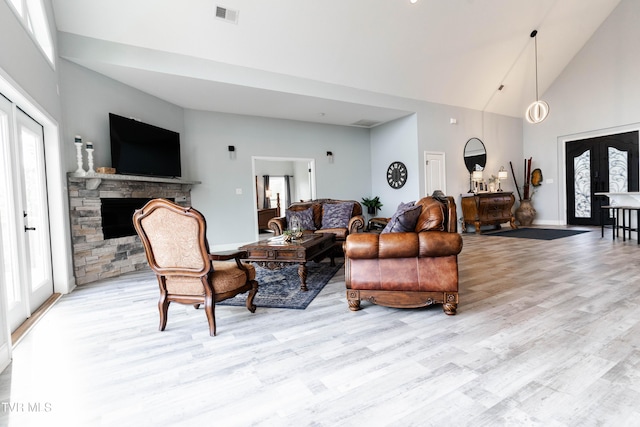 living room featuring high vaulted ceiling, light hardwood / wood-style floors, a stone fireplace, and a healthy amount of sunlight