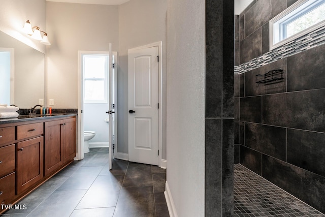 bathroom featuring a tile shower, tile patterned flooring, vanity, and toilet