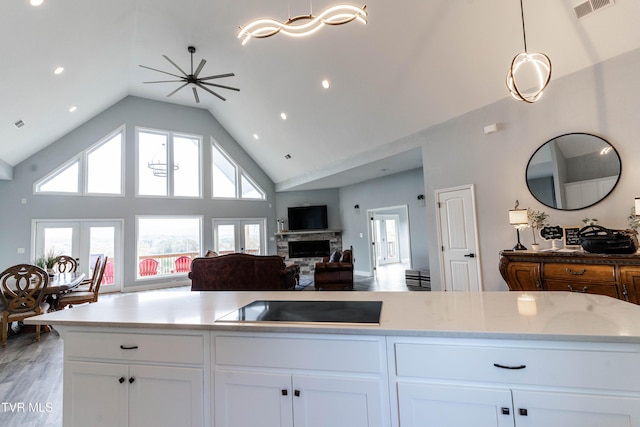 kitchen with a fireplace, black electric cooktop, white cabinetry, and hanging light fixtures