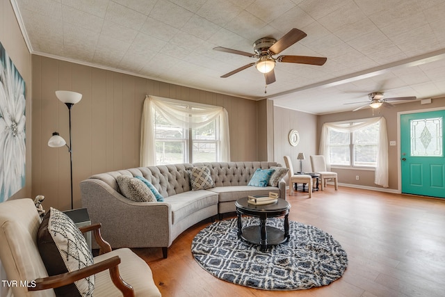 living room with ornamental molding, wood walls, hardwood / wood-style flooring, and ceiling fan