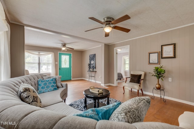 living room with ornamental molding, ceiling fan, wooden walls, and light hardwood / wood-style floors