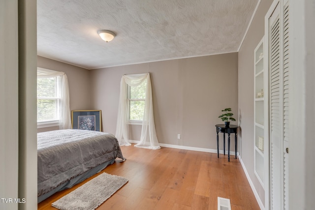 bedroom featuring light wood-type flooring, a textured ceiling, and crown molding