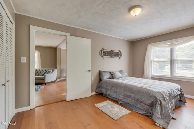 bedroom featuring light hardwood / wood-style floors, a textured ceiling, crown molding, and a closet