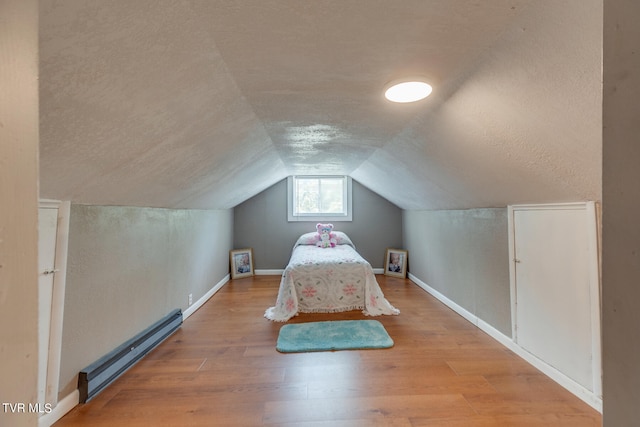 unfurnished bedroom with a baseboard heating unit, light hardwood / wood-style flooring, a textured ceiling, and vaulted ceiling