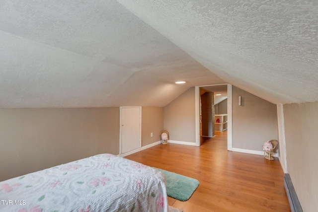 bedroom with wood-type flooring, a textured ceiling, and vaulted ceiling