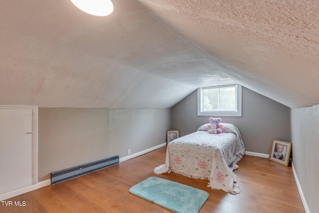 bedroom with hardwood / wood-style flooring, baseboard heating, a textured ceiling, and lofted ceiling