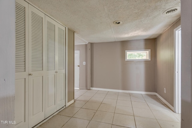 corridor featuring wooden walls, a textured ceiling, and light tile patterned flooring