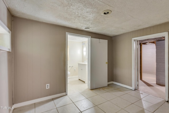 unfurnished bedroom featuring ensuite bath, light tile patterned floors, a textured ceiling, and wooden walls