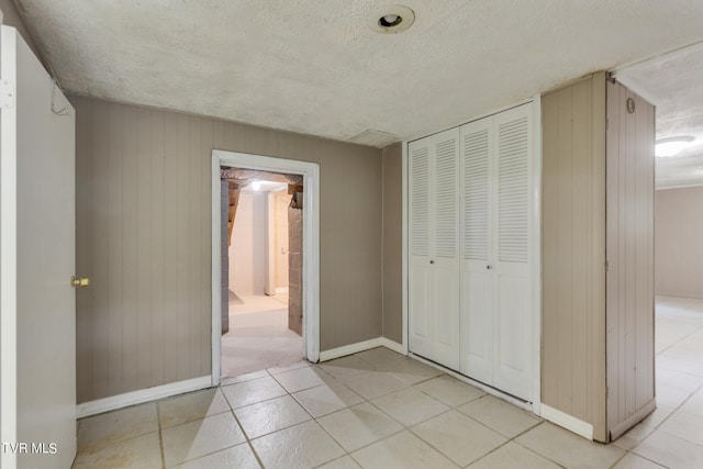 unfurnished bedroom with a closet, light tile patterned flooring, a textured ceiling, wood walls, and ensuite bathroom