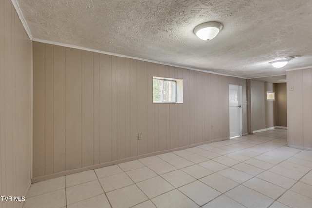 tiled spare room with a textured ceiling, ornamental molding, and wooden walls