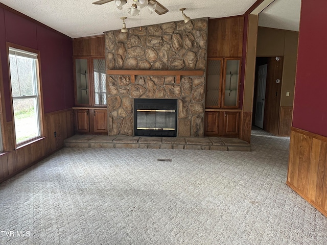 unfurnished living room featuring a stone fireplace, a textured ceiling, vaulted ceiling, light colored carpet, and ceiling fan